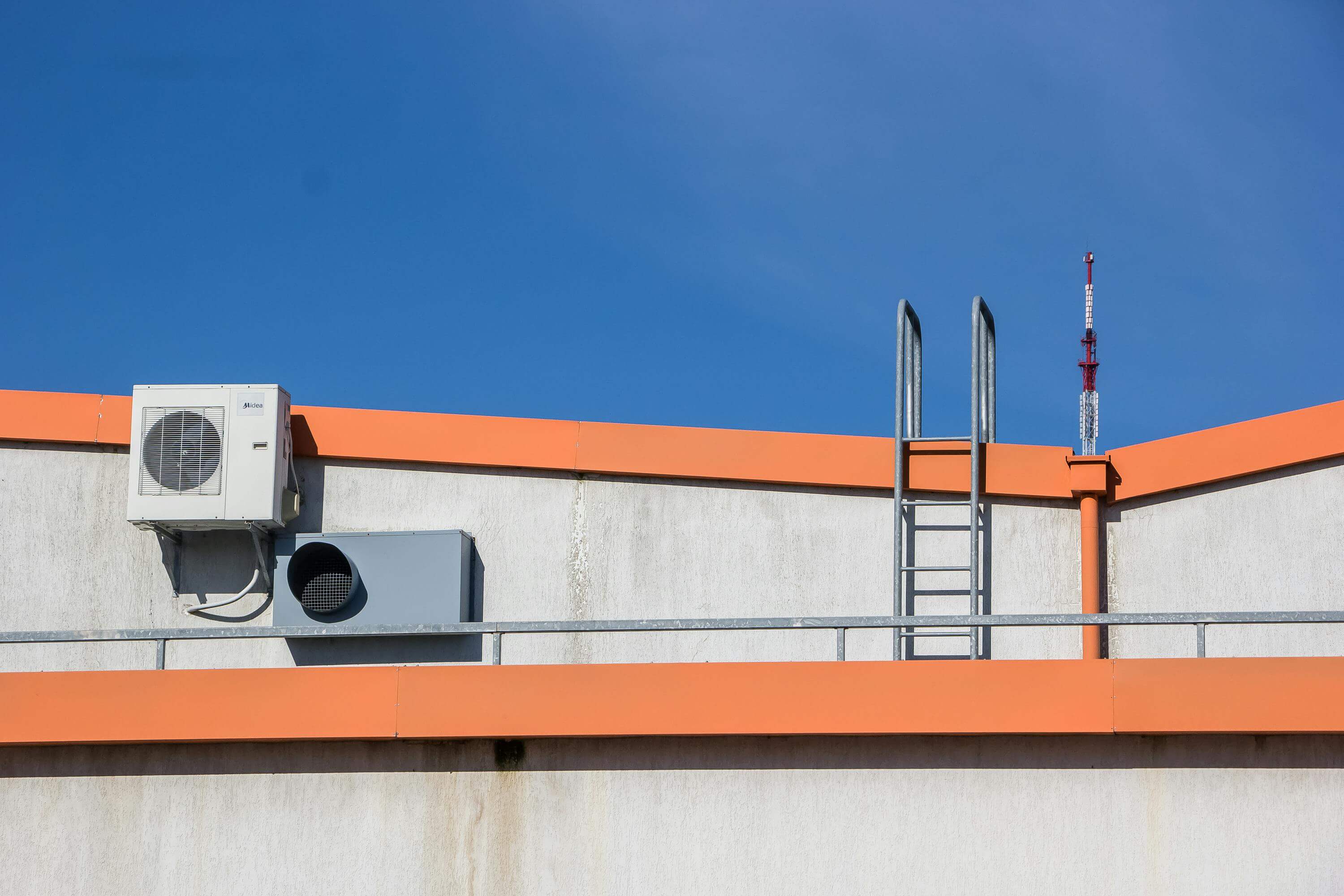Rooftop with antennas, air conditioner, and a clear blue sky.