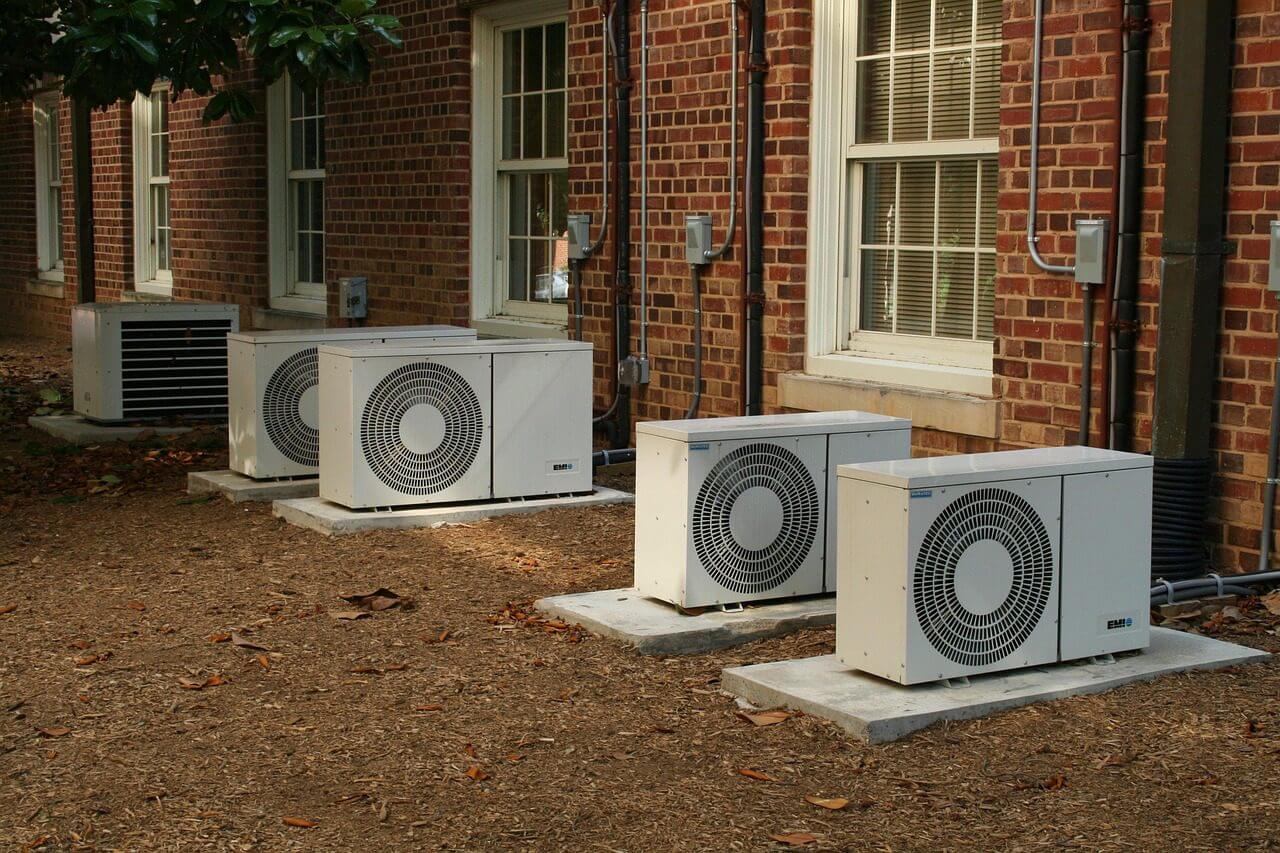 Three outdoor air conditioning units installed beside a brick building.