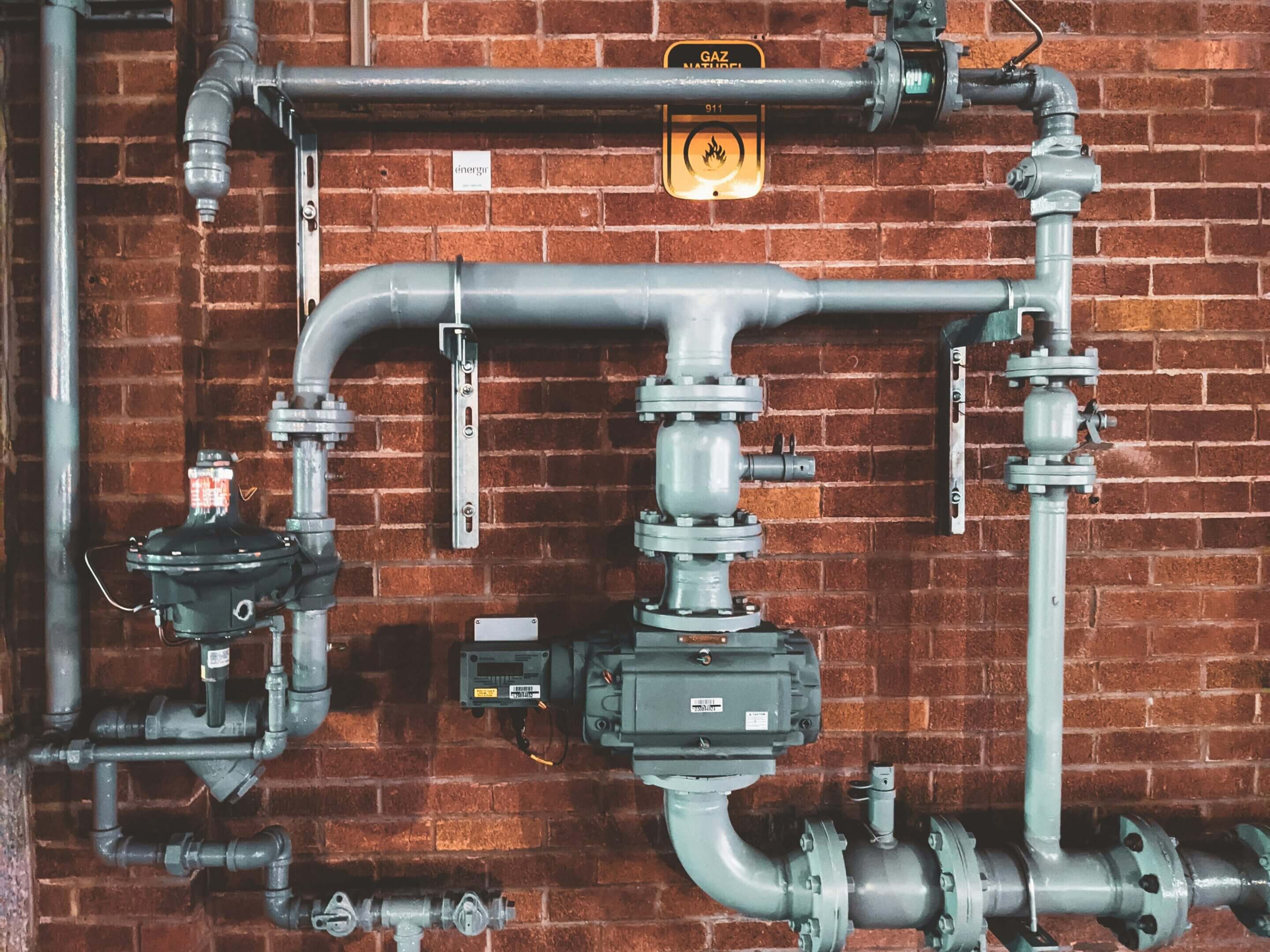 Industrial pipes and meters mounted on a red brick wall.