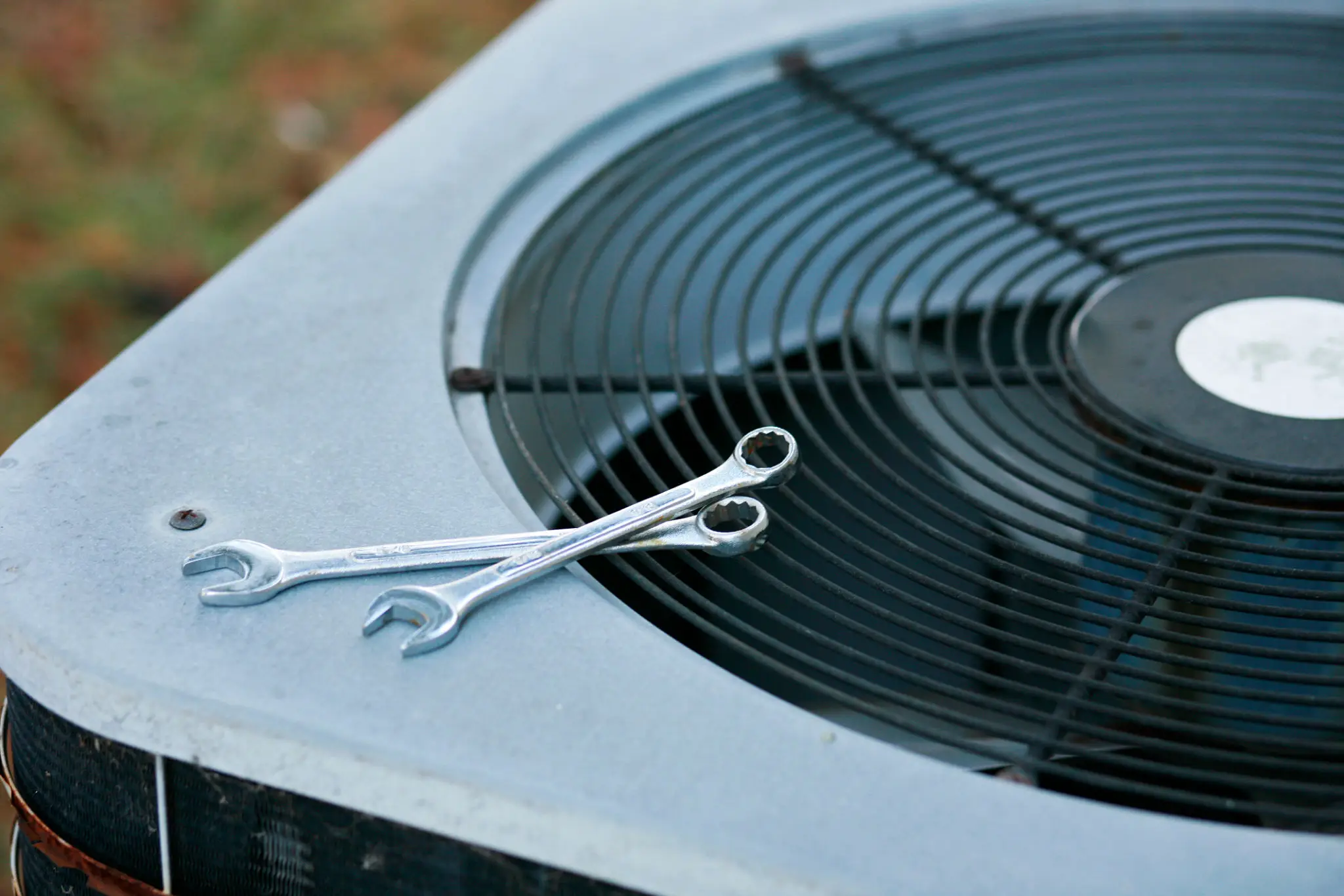 Two wrenches resting on an air conditioning unit's fan grille.