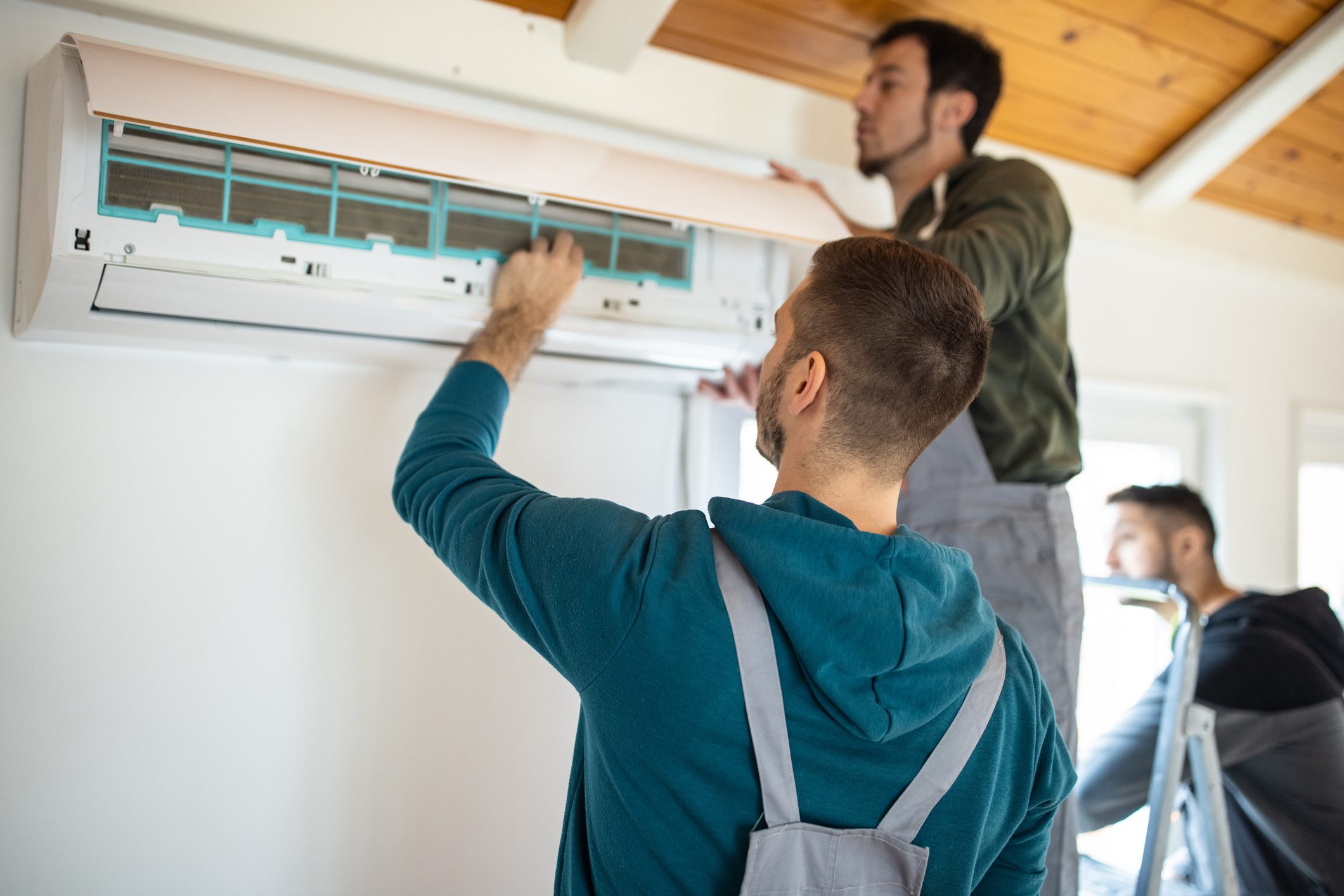 Technicians repairing a wall-mounted air conditioner.